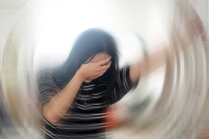 Woman holding her head in distress with a blurred, swirling background, depicting the disorienting effects of anxiety and the need for anxiety treatment.