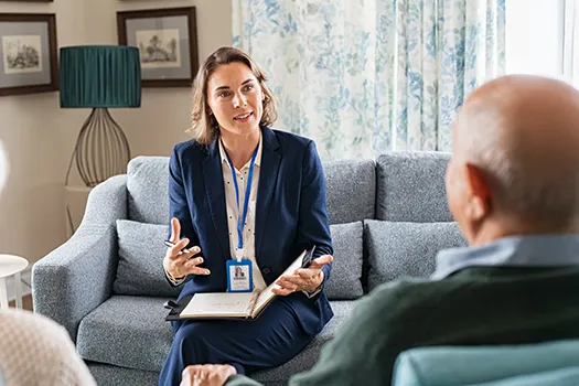 A compassionate female mental health professional, dressed in a business suit, actively engaging in a personalized therapy session with an older male patient on a couch, emphasizing individualized mental health care.