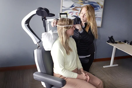 Patient receiving Transcranial Magnetic Stimulation (TMS) therapy, with a technician adjusting the coil, for mental health treatment.