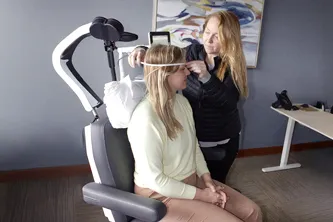 Patient receiving Transcranial Magnetic Stimulation (TMS) therapy, with a technician adjusting the coil, for mental health treatment.