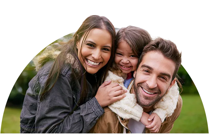 A smiling family with a mother, a father, and a small child on the father's back.