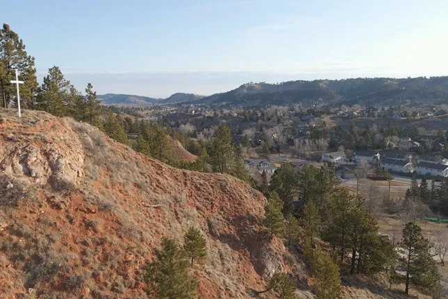 MWI Health in Rapid City, South Dakota. Scenic view of the city from a hill with a white cross and trees, representing a key local landmark.