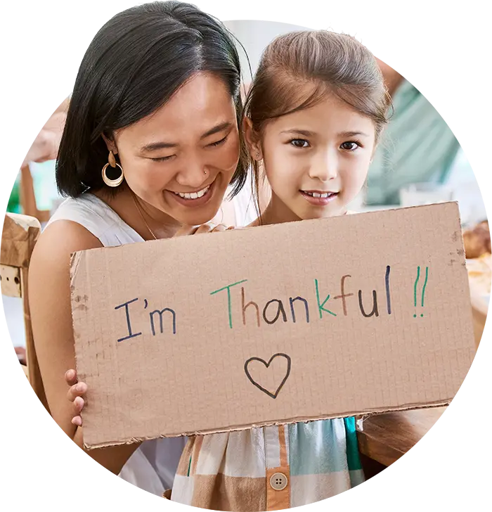 A close-up of a smiling mother and young daughter connecting while holding a handwritten cardboard sign that reads, "I'm Thankful !!" This image symbolizes the clarity and emotional presence possible when prioritizing mental wellness for a joyful holiday season.