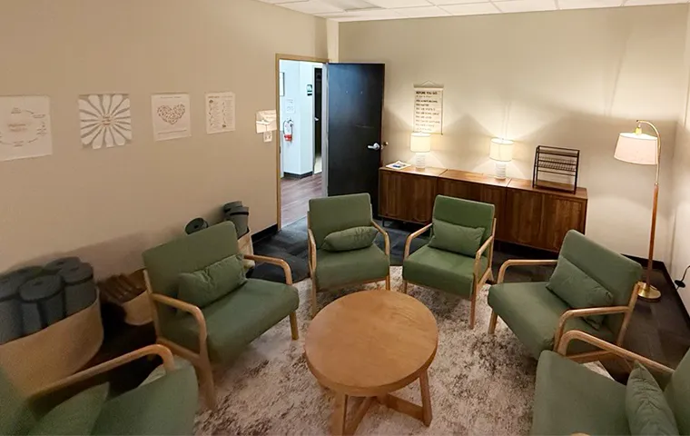Group therapy room at SMHWI Rockwall IOP featuring green armchairs arranged in a circle with a round wood coffee table and wellness artwork on the walls