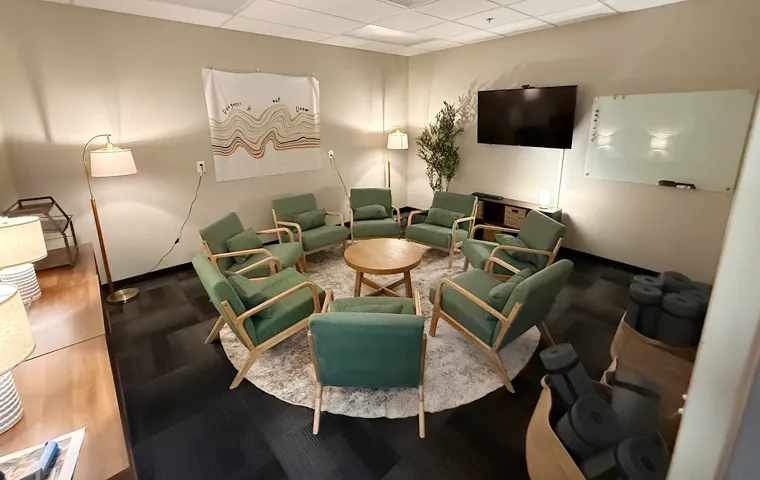 Group therapy room at SMHWI Rockwall IOP with green armchairs in a full circle, wall-mounted TV, whiteboard, and decorative wall art